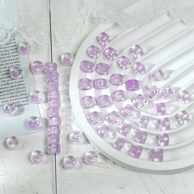 Lavender glitter barrel beads on a white spiral tray with a beaded strand and loose beads on a white surface