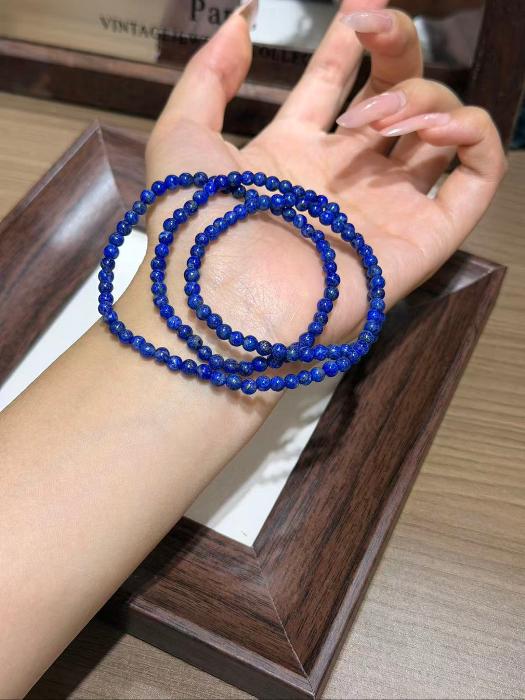 Triple-wrapped deep royal blue beaded bracelet worn on a wrist above a dark wooden tray.