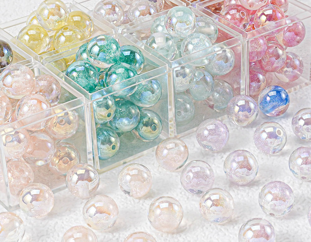 Iridescent round craft beads in pastel colors arranged in clear plastic compartments and scattered on a white surface.
