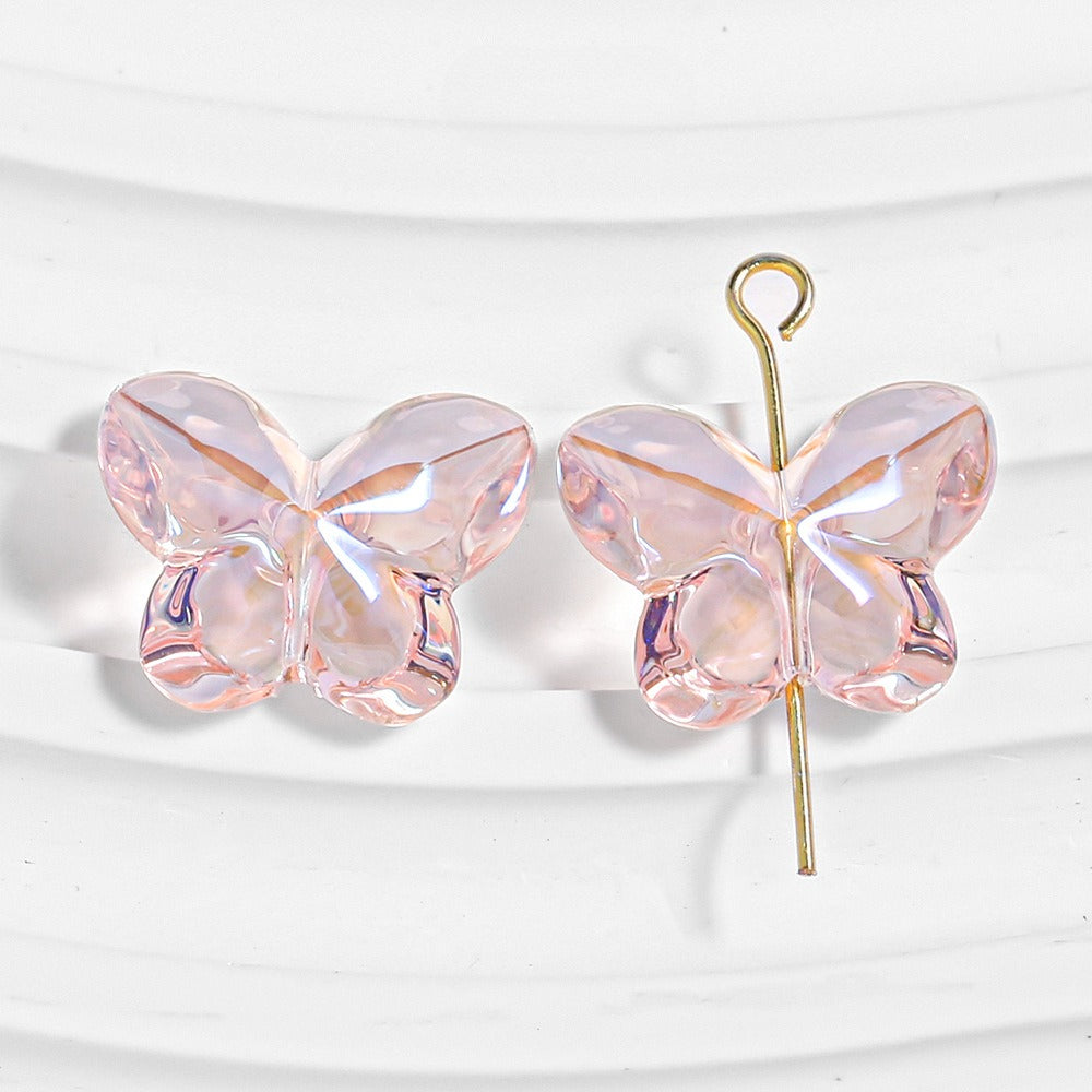 Two pink faceted butterfly-shaped beads, one threaded on a gold headpin, on a white wavy background