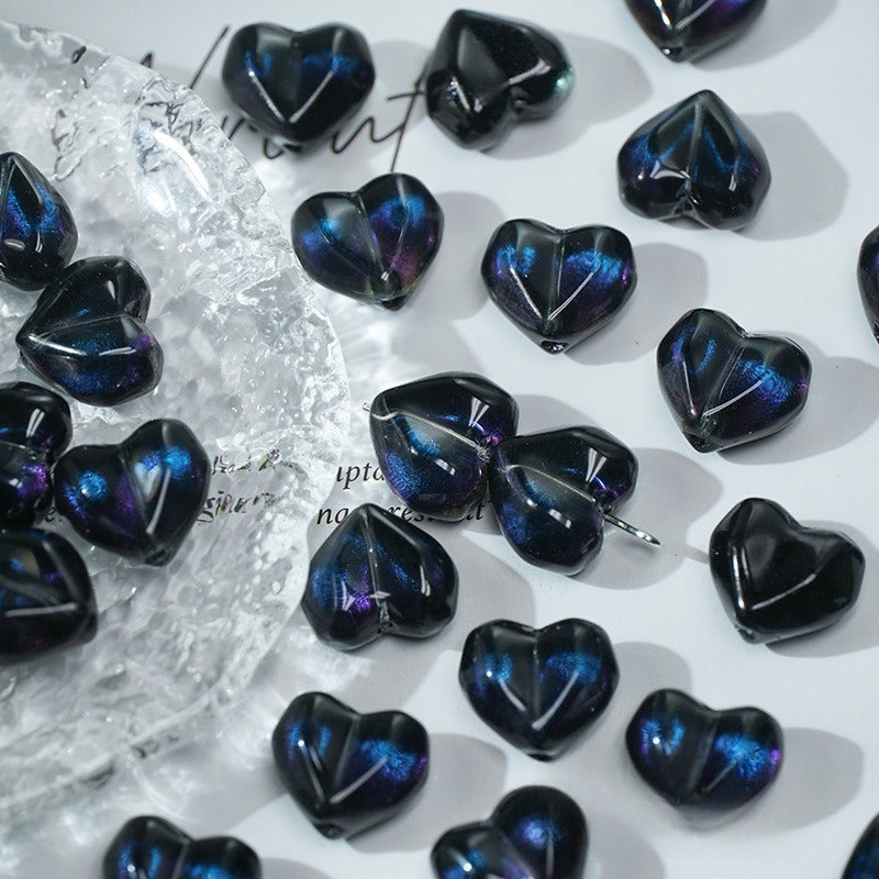 Dark metallic iridescent heart-shaped glass beads with blue and purple tones on a white surface