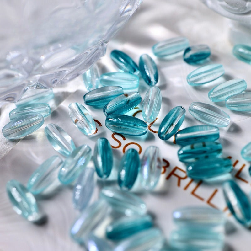 Light blue translucent 4x9mm glazed glass long rice beads scattered on white surface