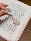 Hand holding pink quartz bear phone charm with crystal beads over an open book