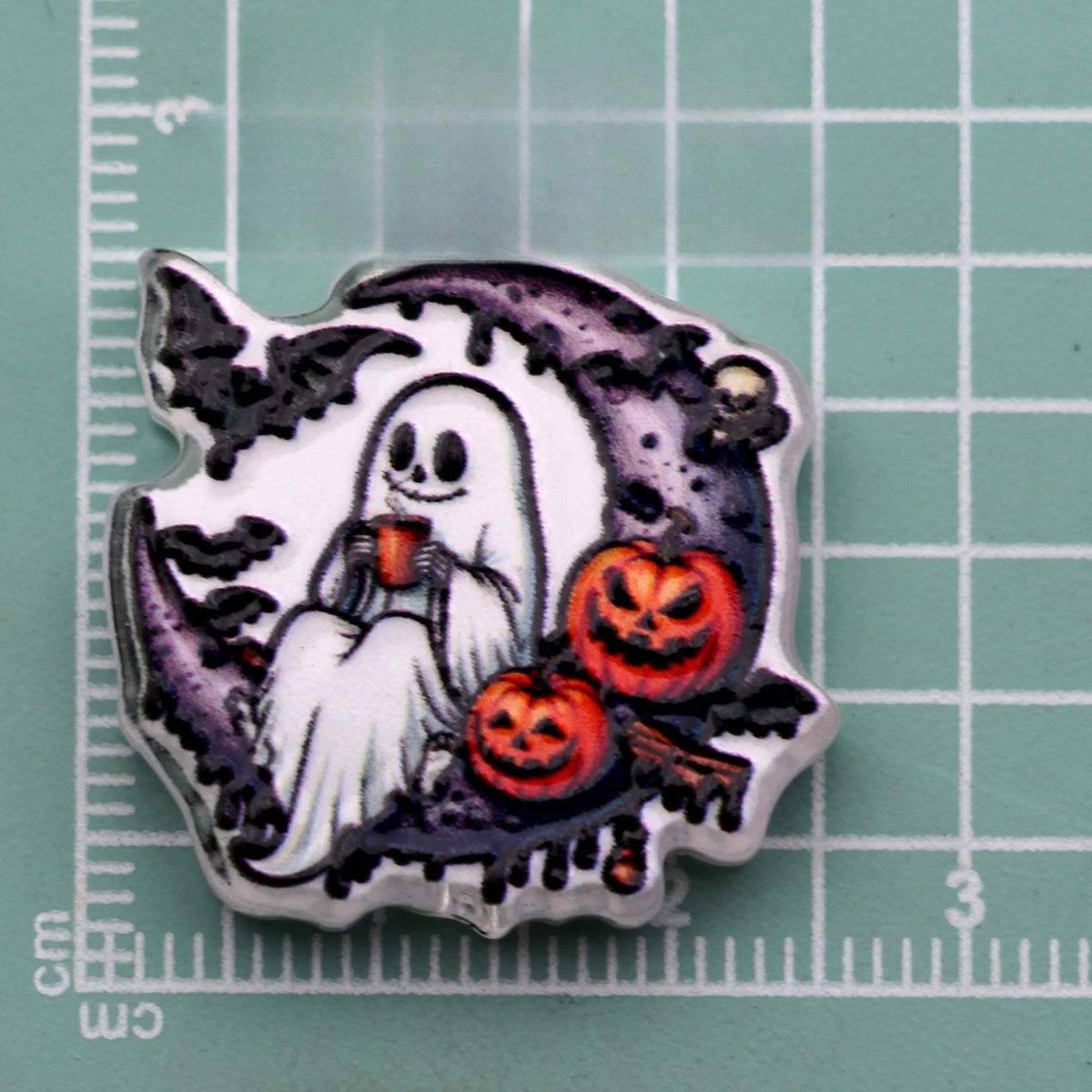 Halloween acrylic bead with a ghost holding a mug on a crescent moon with pumpkins and bats on a cutting mat