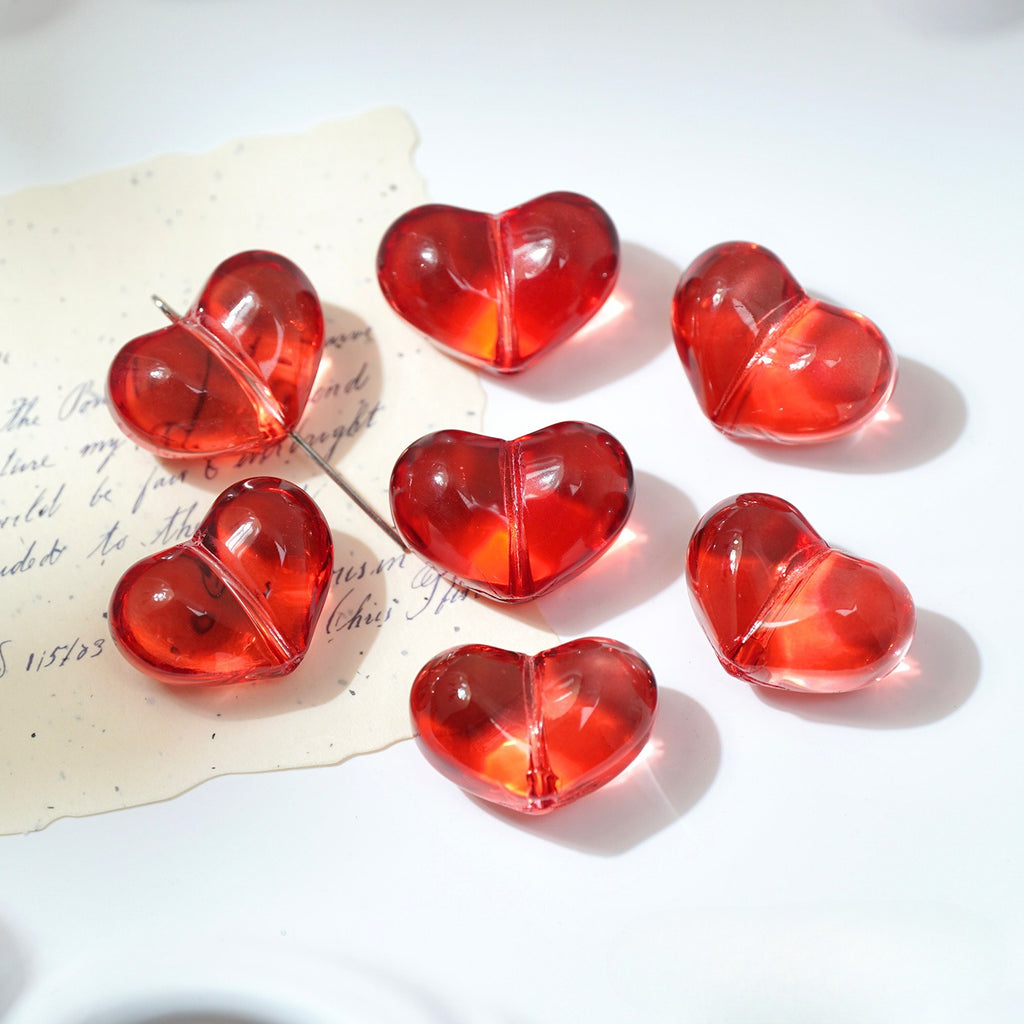 Seven translucent red heart-shaped glass beads on a white surface