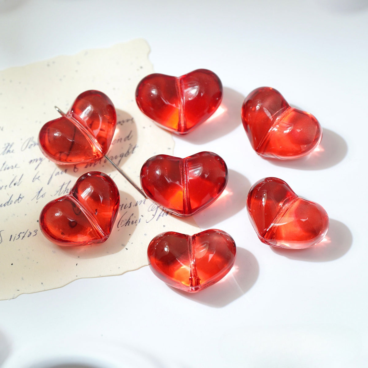 Seven translucent red heart-shaped glass beads on a white surface