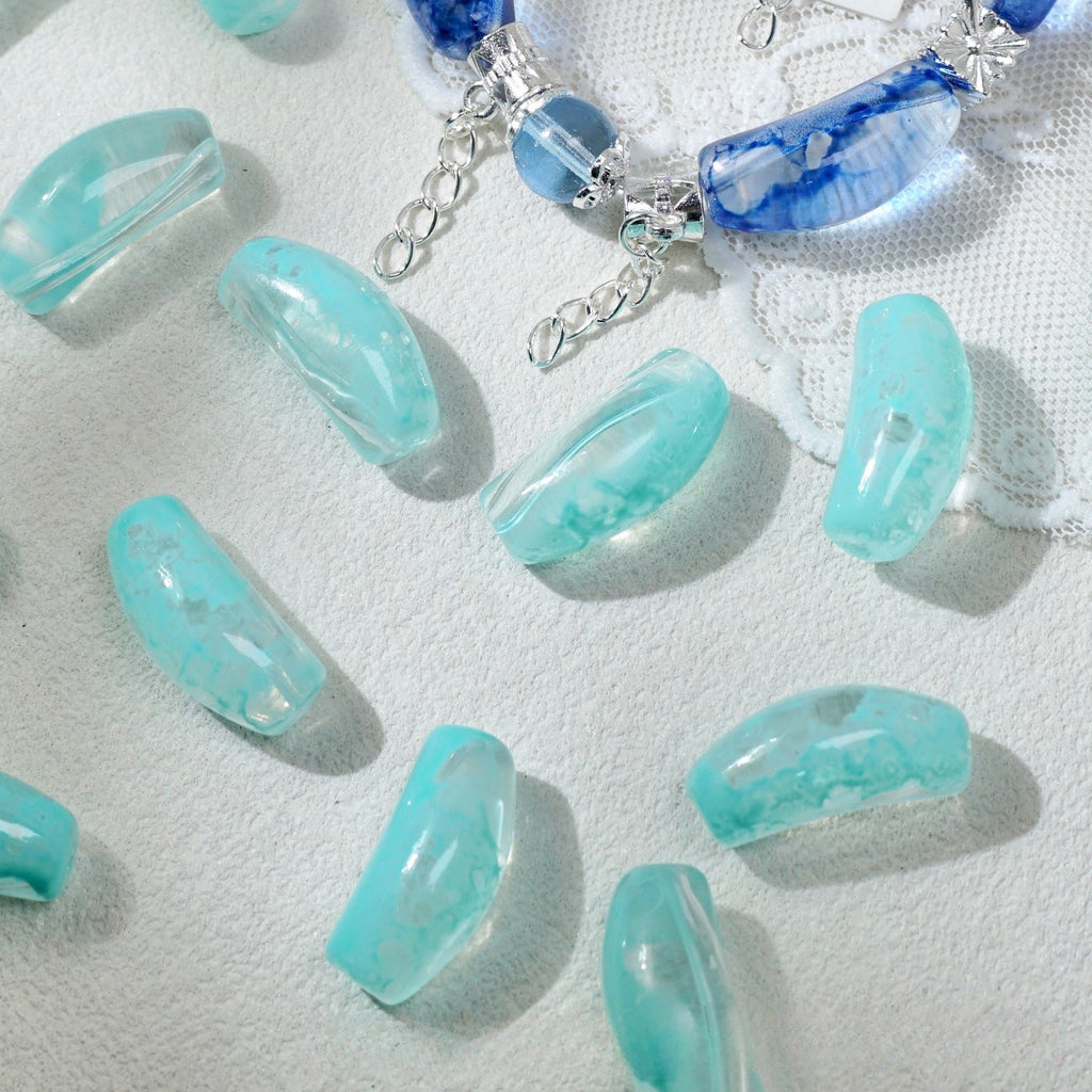 Translucent aqua blue marbled curved glass tube beads scattered on white textured fabric