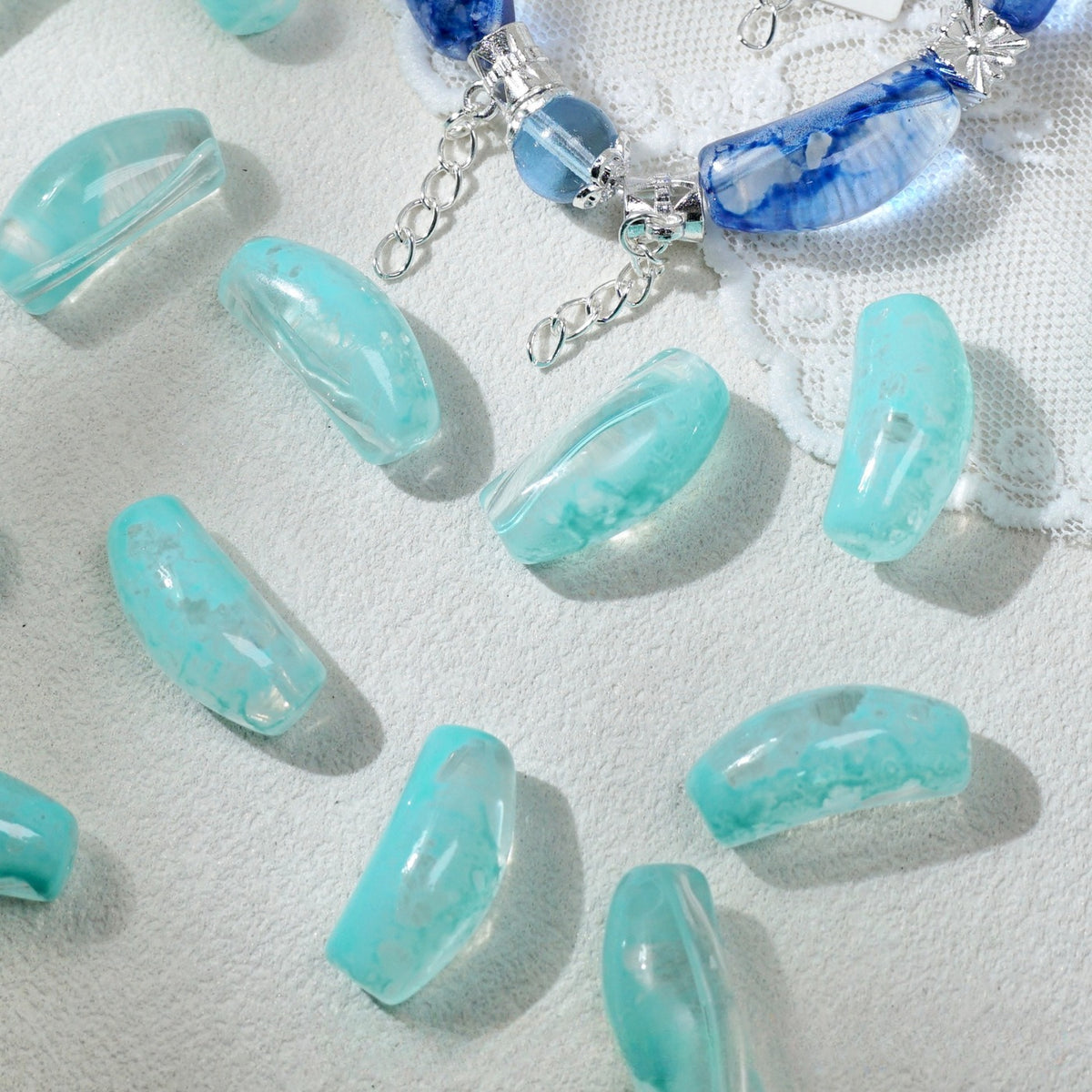 Translucent aqua blue marbled curved glass tube beads scattered on white textured fabric