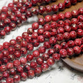 Red porcelain beads with gold foil threads, arranged in strands on a light surface with a wooden tray.