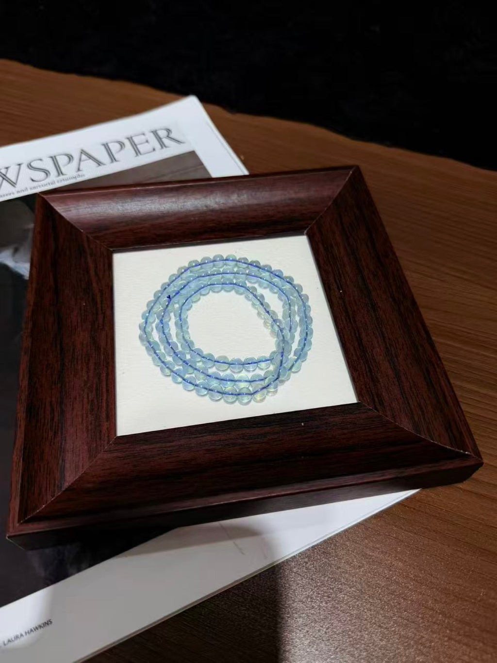 Aquamarine triple-wrap bracelet coiled in a circle on a wooden picture frame over newspaper