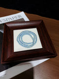 Aquamarine triple-wrap bracelet coiled in a circle on a wooden picture frame over newspaper