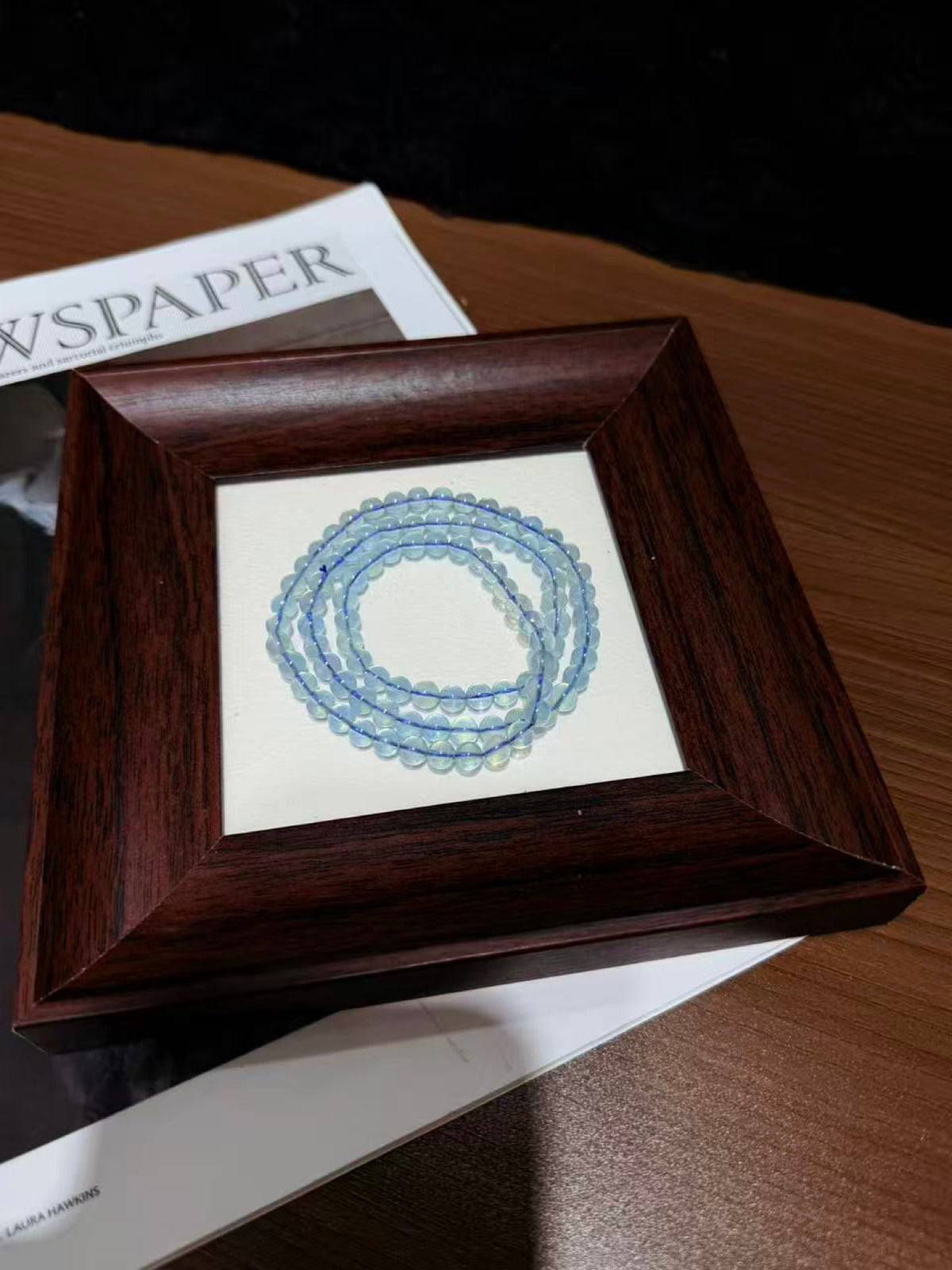 Aquamarine triple-wrap bracelet coiled in a circle on a wooden picture frame over newspaper