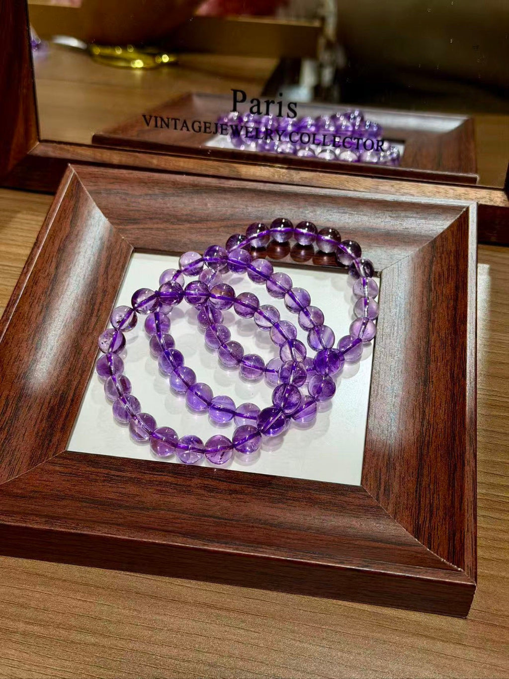Purple amethyst beaded bracelet coiled in a dark wooden display tray, mirror reflecting it behind