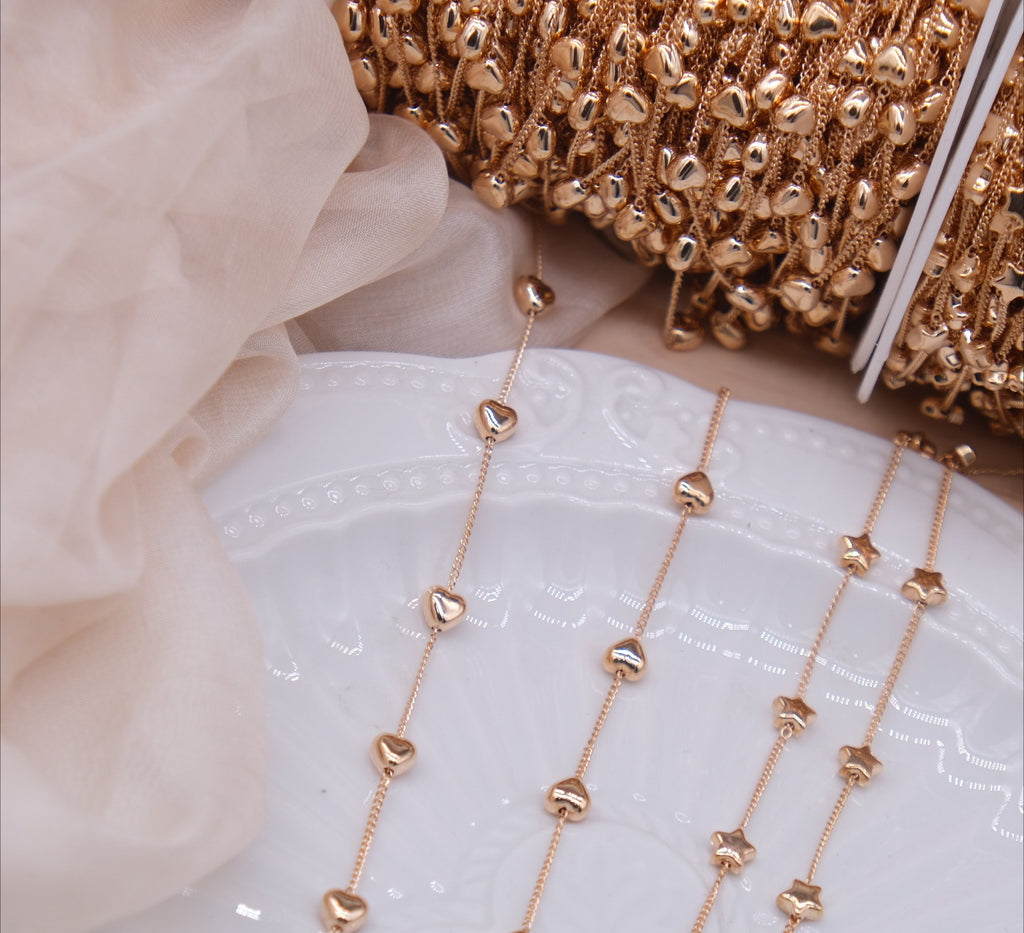 Rose gold heart and star bead chains laid out on a white ceramic plate with spools of chain