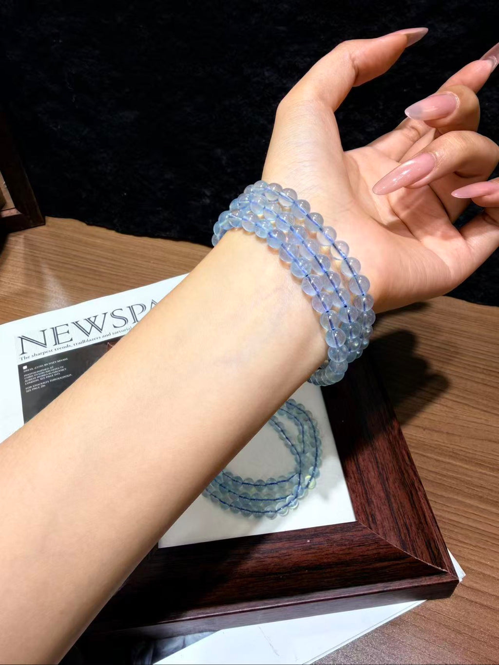 Pale blue aquamarine beaded bracelet worn wrapped around a wrist above a wooden picture frame