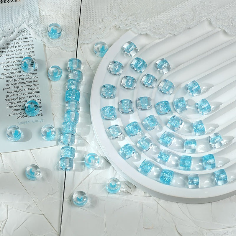Light blue glitter barrel beads on a white ridged tray with loose beads and printed paper nearby