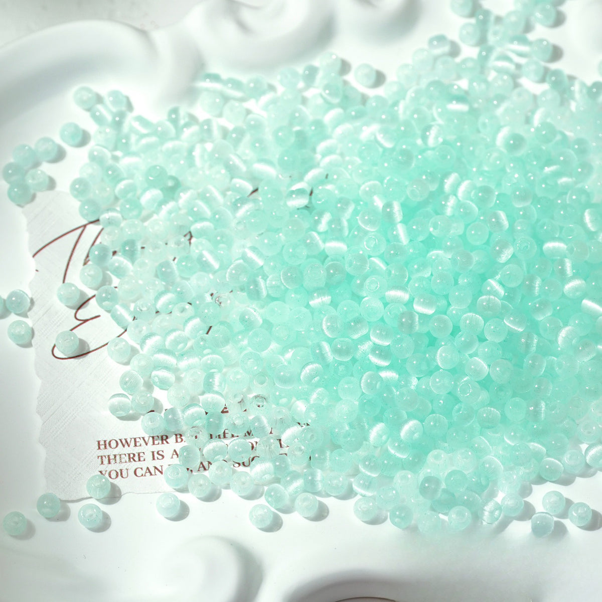 Close-up pile of frosted light-aqua cat's-eye glass beads on white surface