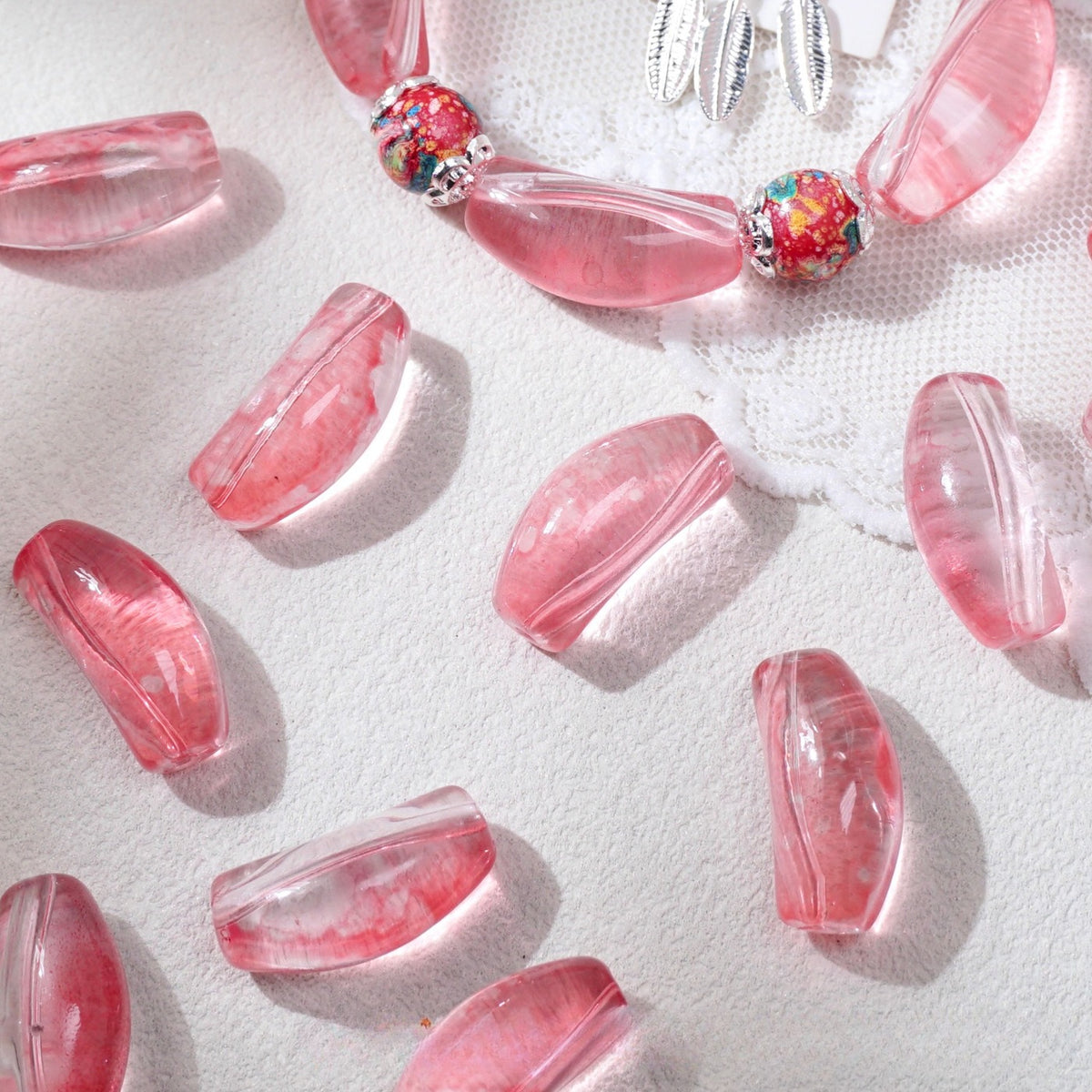 Pink translucent curved glass tube beads scattered on white textured fabric with a partial beaded necklace at the top