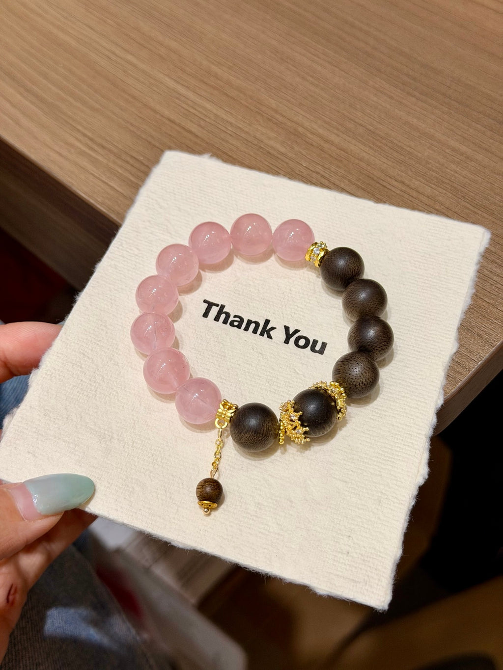 Hand holding pink quartz and sandalwood bracelet with gold dangle accent