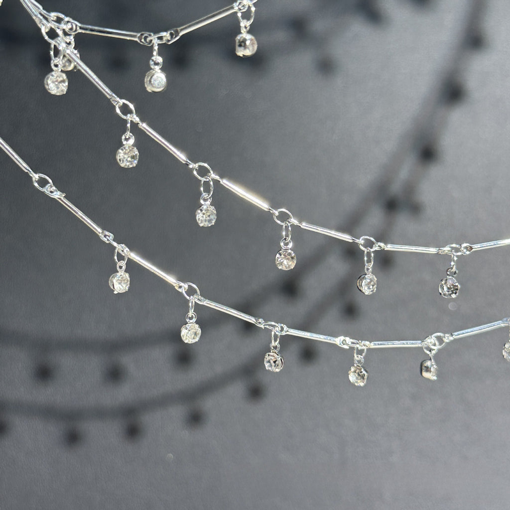 Silver-toned chain necklace with multiple small clear faceted gemstone dangles, photographed close-up against a dark gray background.