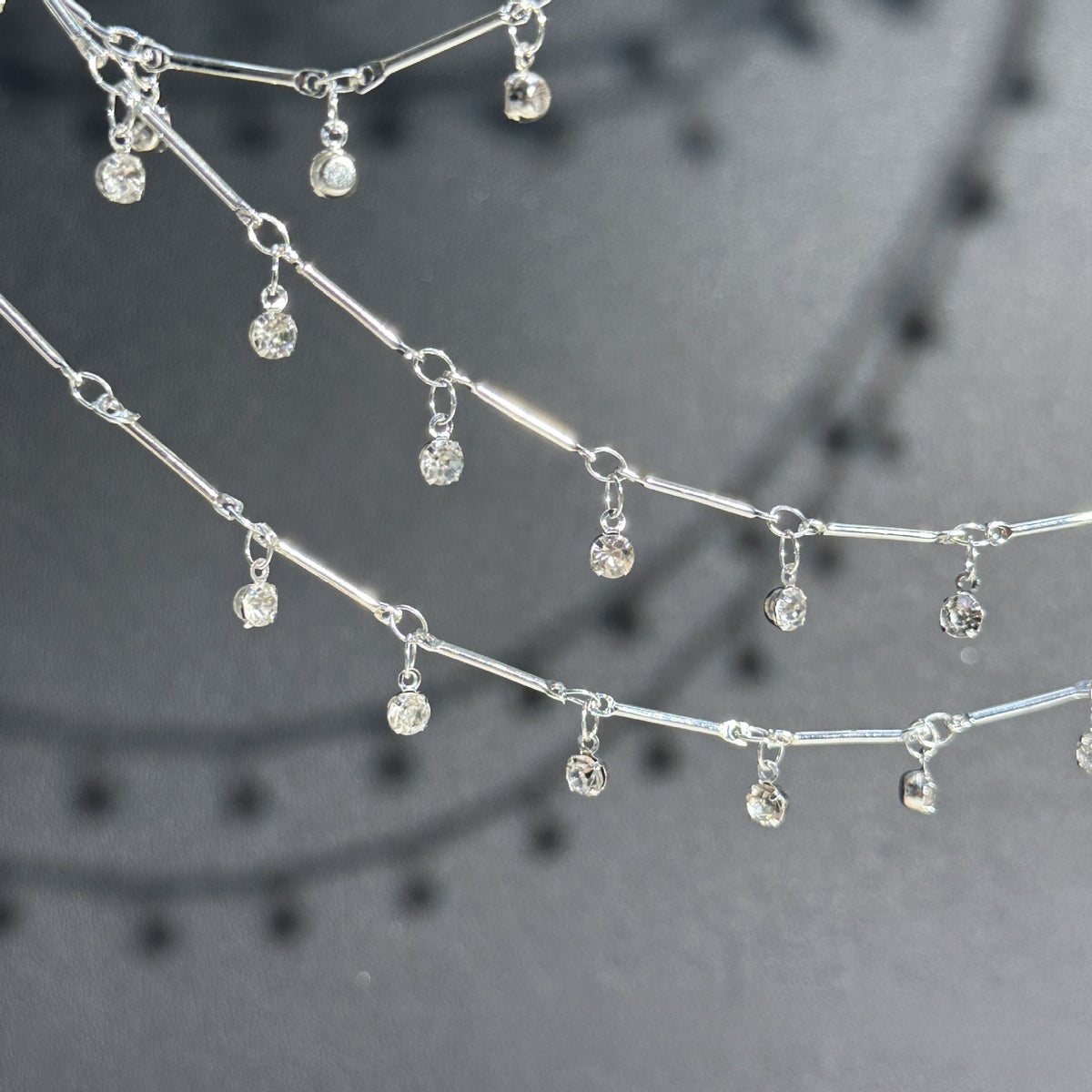Silver-toned chain necklace with multiple small clear faceted gemstone dangles, photographed close-up against a dark gray background.