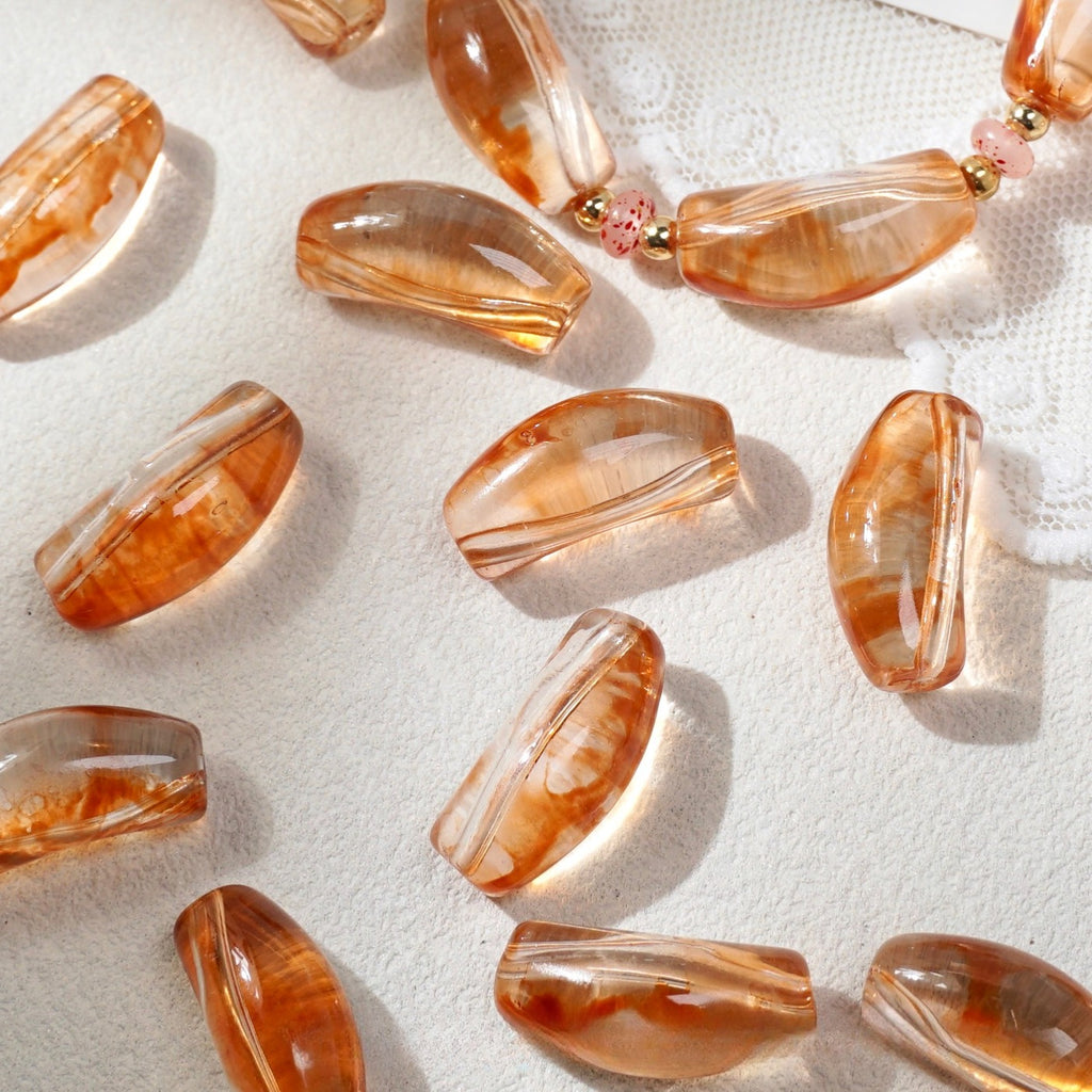 Translucent peach-orange curved glass tube beads with white marbled streaks on white fabric