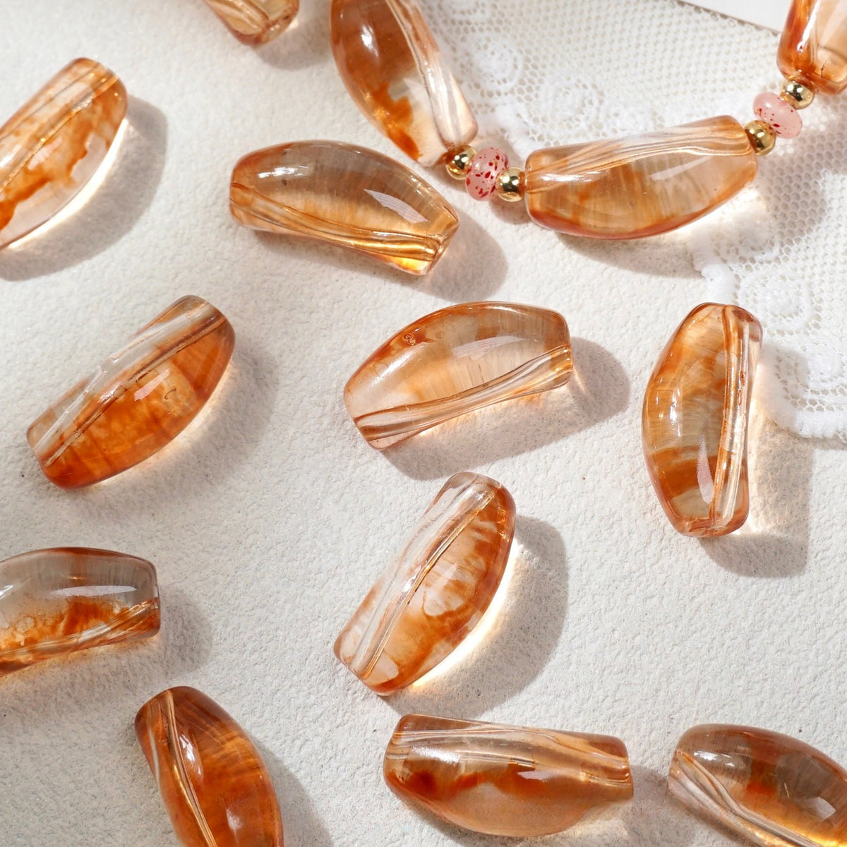 Translucent peach-orange curved glass tube beads with white marbled streaks on white fabric