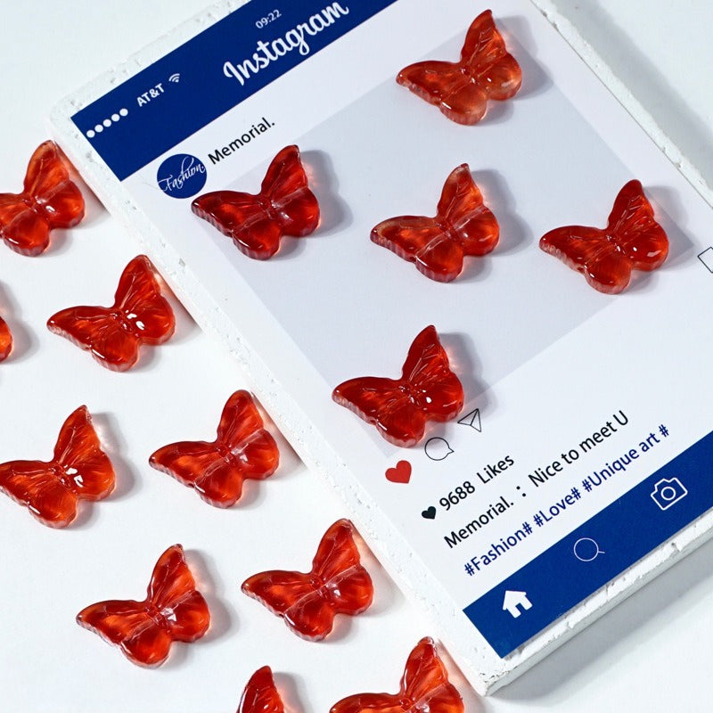 Red translucent butterfly-shaped glass beads on a white surface next to an Instagram post card