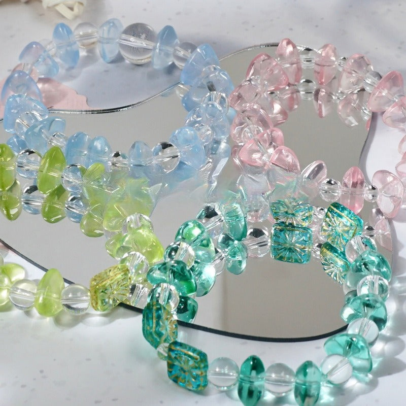 Pastel blue, pink, green and teal beaded bracelets with clear beads arranged on a reflective mirror