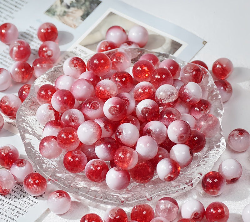 Red and white gradient glass beads scattered on a white surface with a clear glass dish in the center holding the beads.
