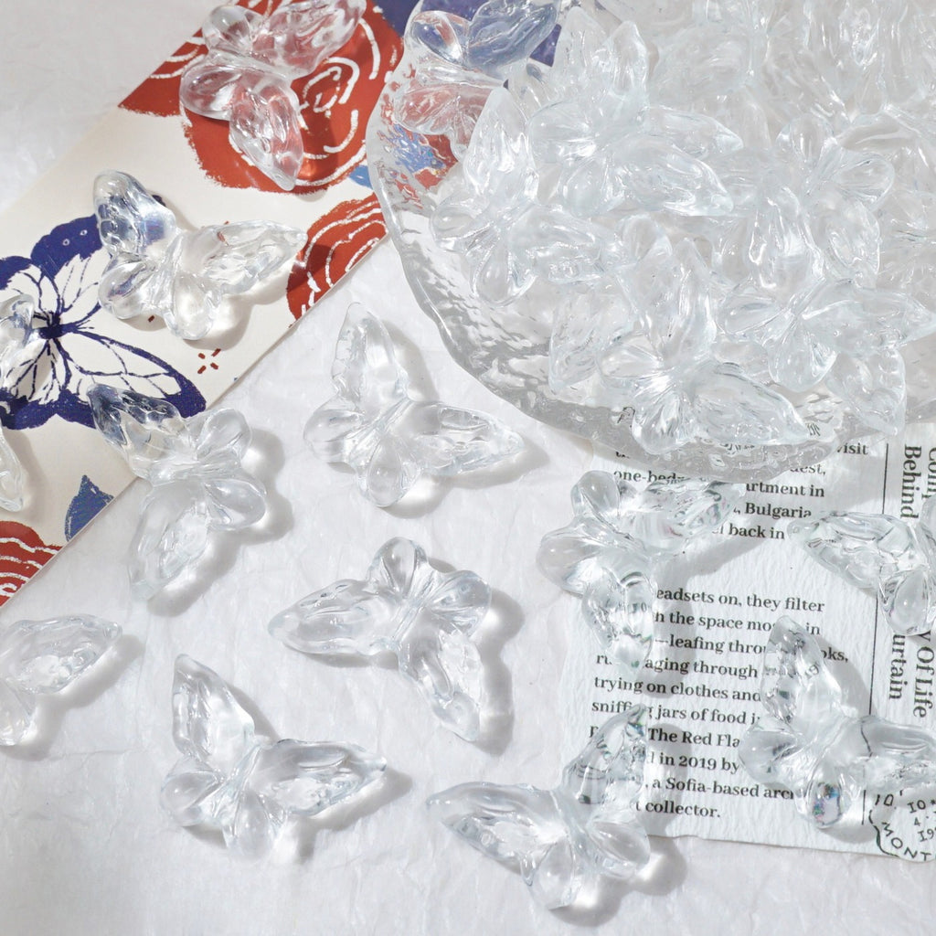 Clear butterfly-shaped glass beads scattered on white textured surface with matching clear glass bowl