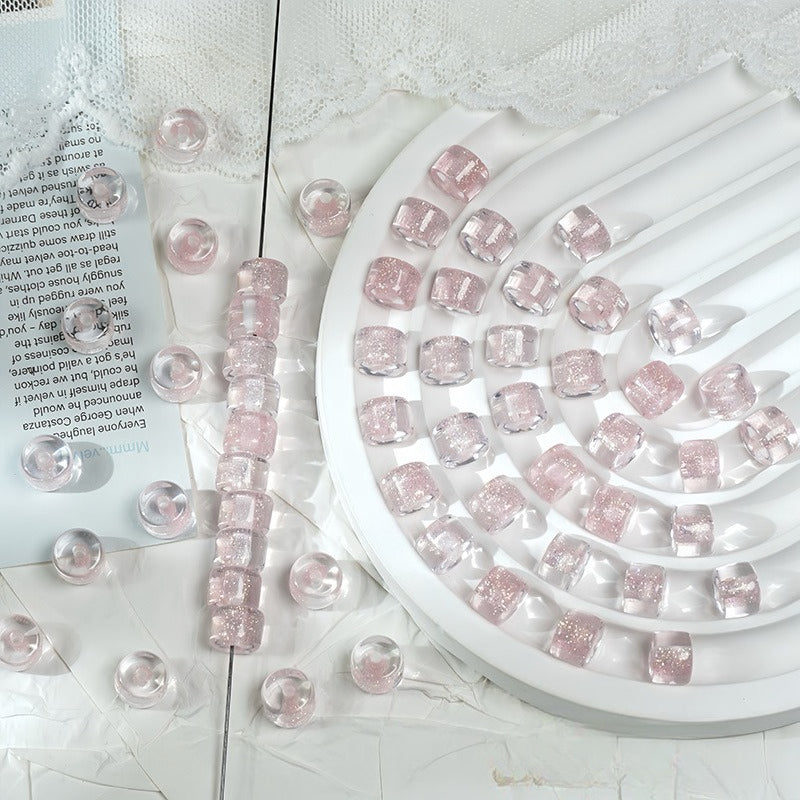 Pink glittery barrel beads on a white spiral tray, some scattered on a white surface with lace and paper props