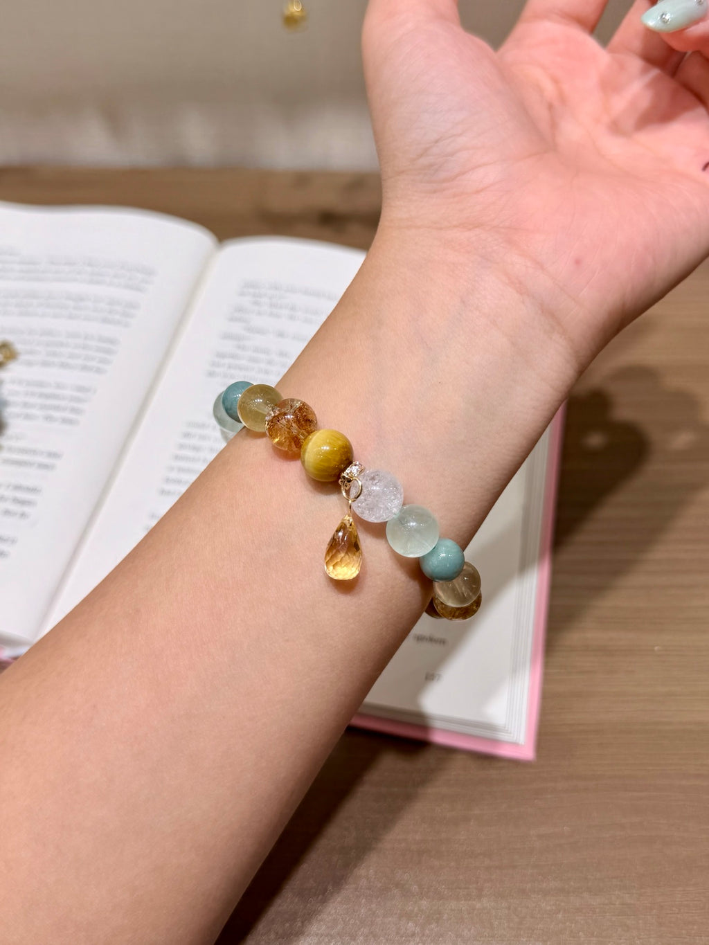 Gilded Dawn multi-stone bracelet with zircon spacers held in hand over open book