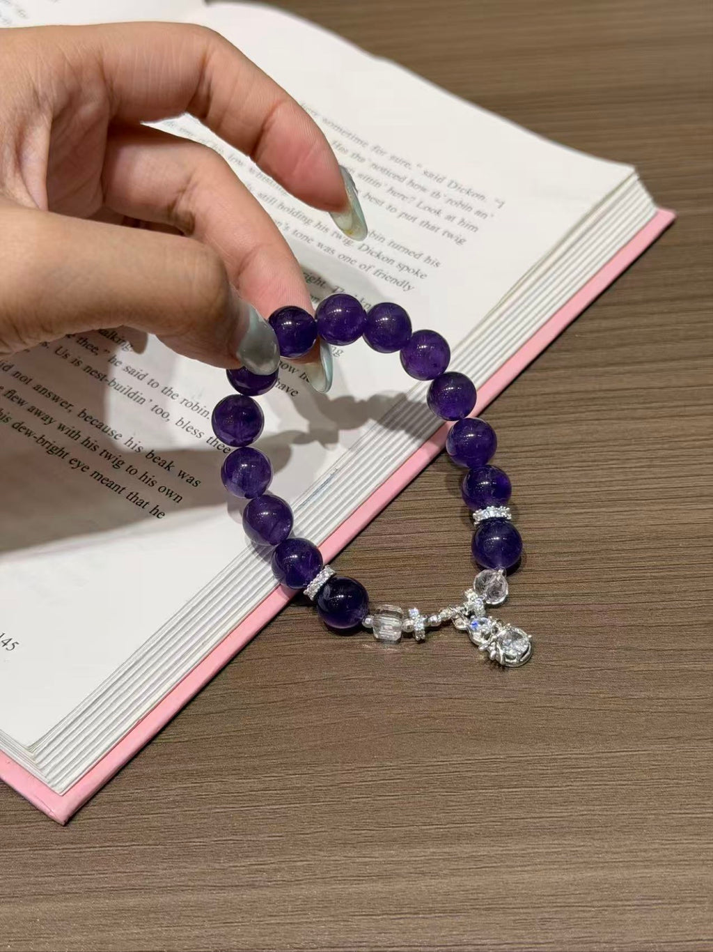 Hand holding amethyst dream bracelet with faceted white crystal over book