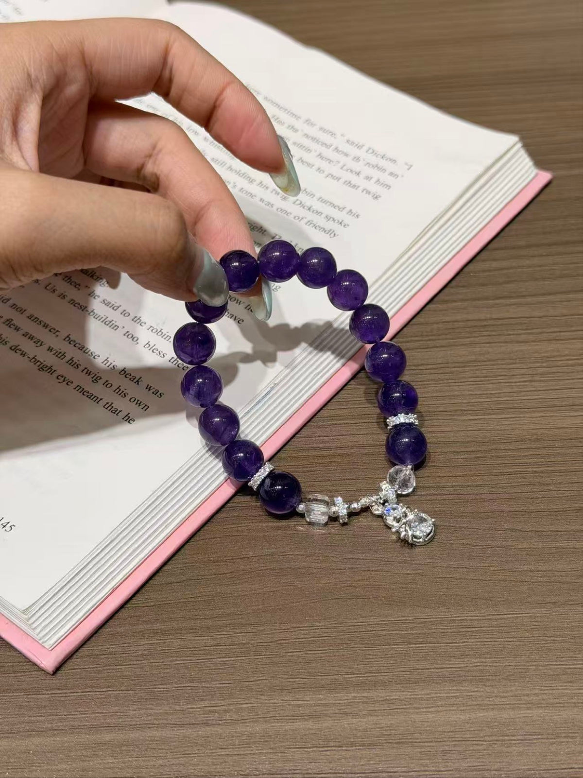 Hand holding amethyst dream bracelet with faceted white crystal over book
