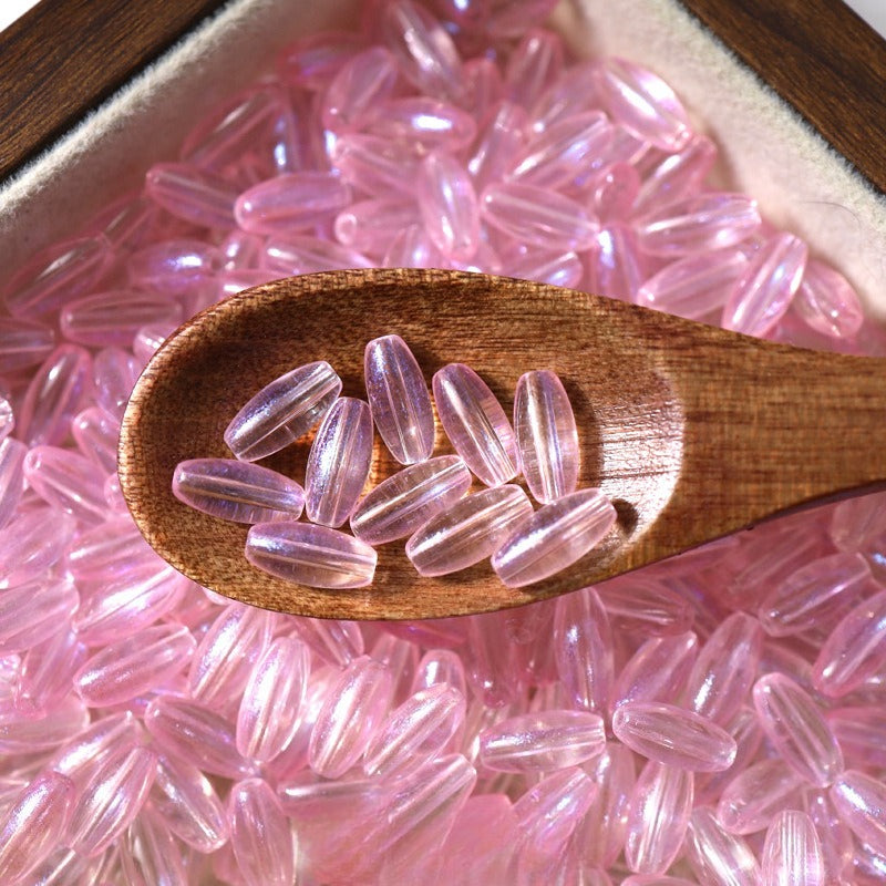 Pink translucent 4x9mm glazed glass long rice beads scattered in a white dish