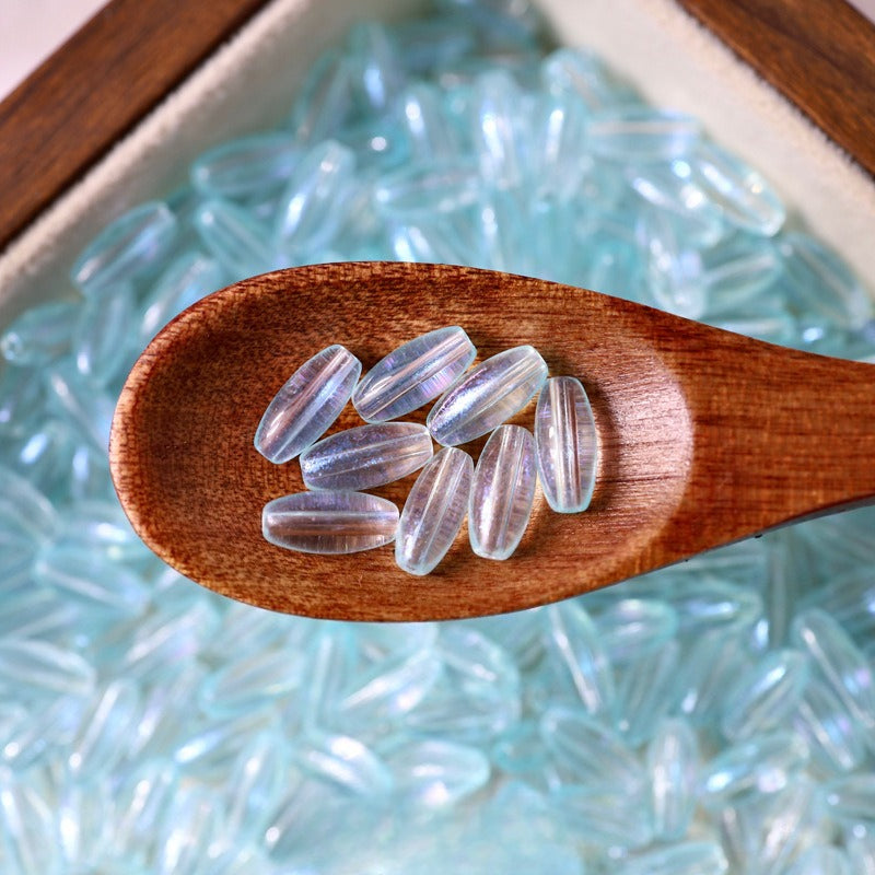 Light blue translucent 4x9mm glazed glass long rice beads in a wooden spoon