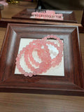 Pink translucent round beaded bracelet coiled in a dark brown wooden frame tray