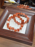 Golden sunstone cube bracelet with translucent peach-orange sugar cube beads coiled on a white insert inside a dark wood display frame