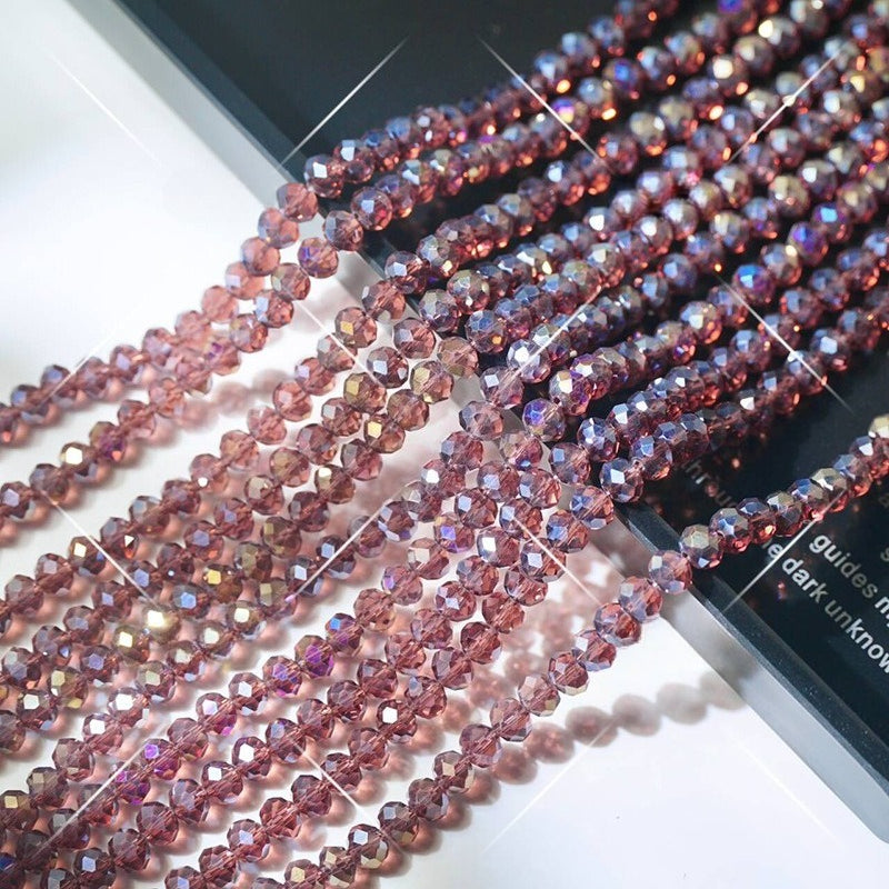 Multiple strands of faceted dusty rose pink crystal glass wheel beads arranged diagonally on white surface