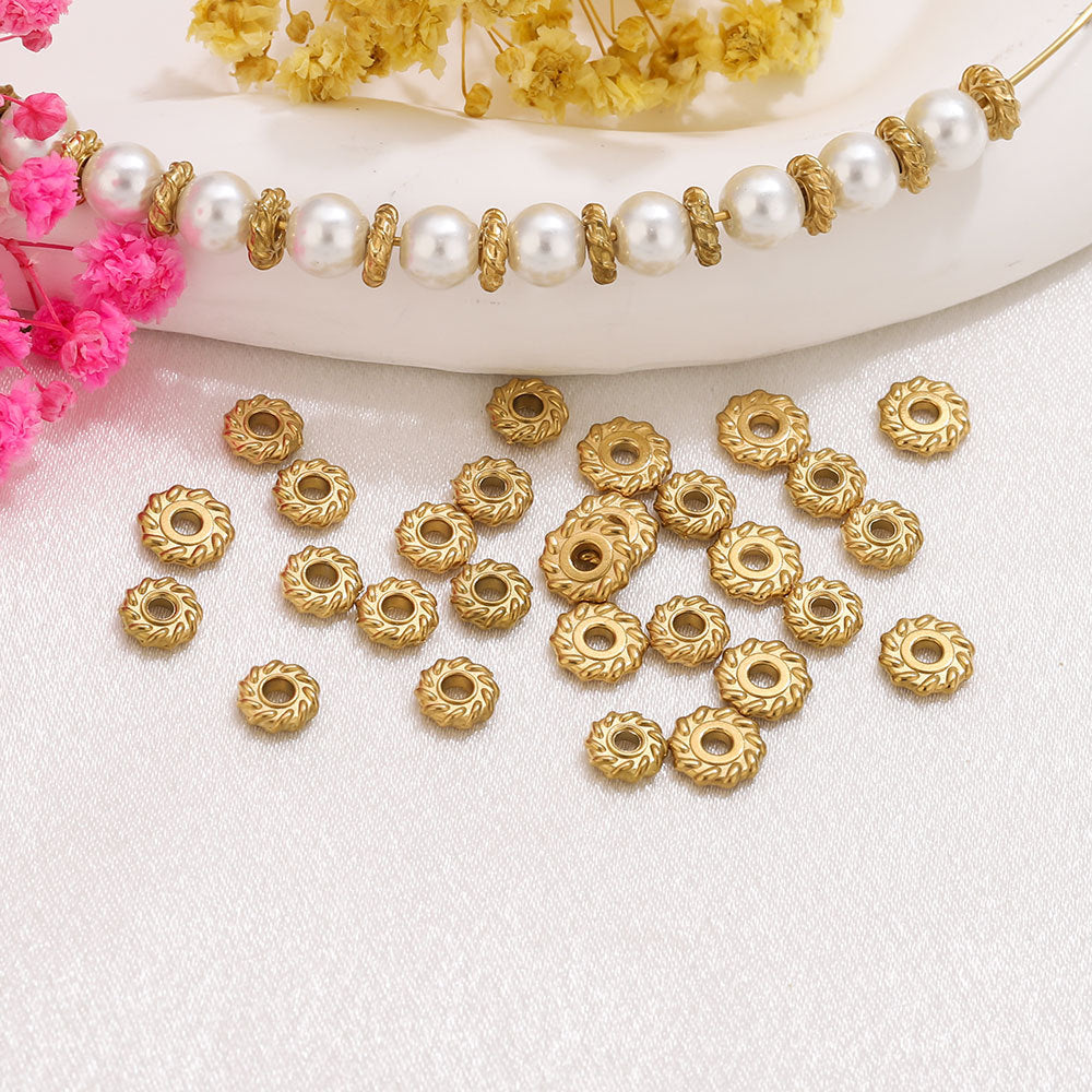 Gold-toned round spacer beads with a textured floral edge scattered on a white fabric surface