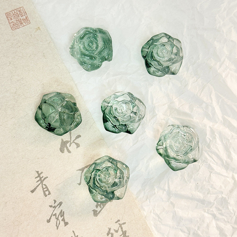 Five faceted green glass rose-shaped beads on a split background of white and beige paper with calligraphy