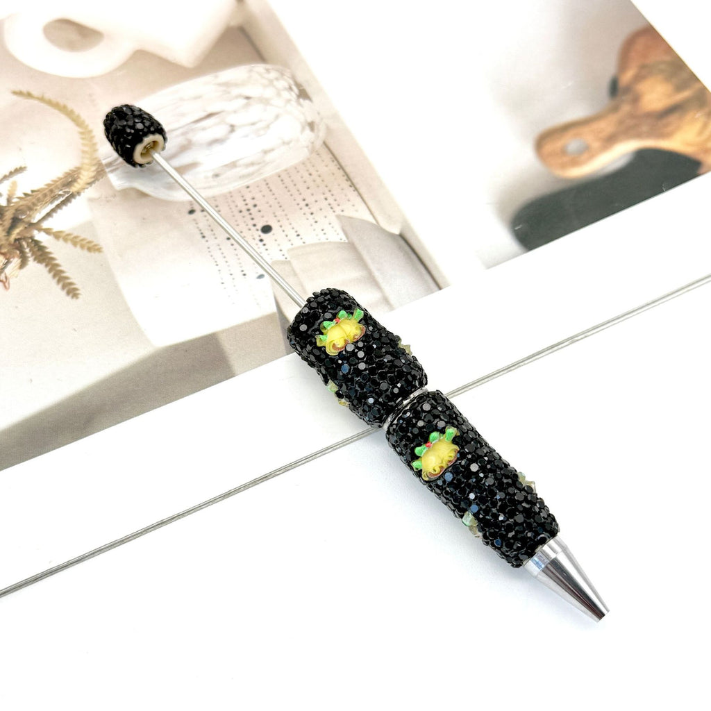 Black rhinestone ballpoint pen with small yellow and green flower embellishments.