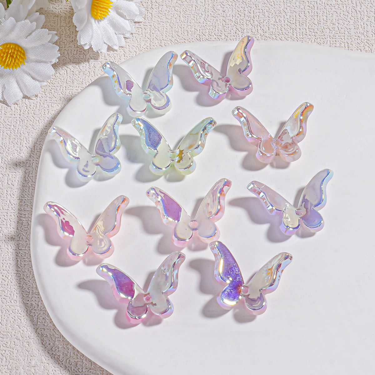 Nine iridescent butterfly acrylic beads on white plate with white daisies