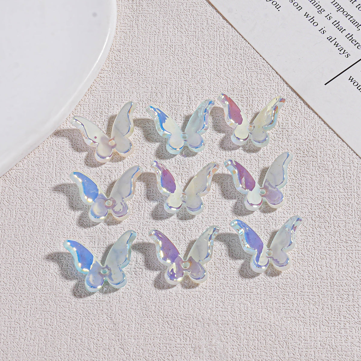 Nine small iridescent butterfly acrylic beads on textured beige surface with white plate and paper edges