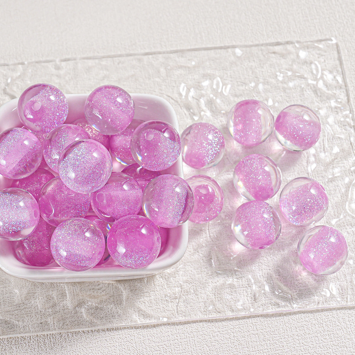 Pink glitter round beads in a white dish and scattered on textured white surface