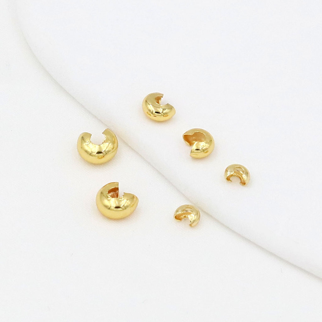 Five small gold C-shaped crimp bead covers scattered on a white background