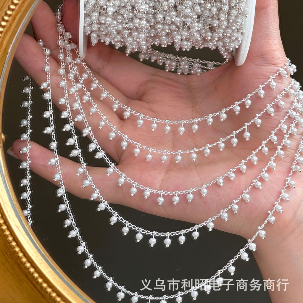 Hand holding silver 3mm white glass pearl chain garland draped across oval mirror with gold frame.