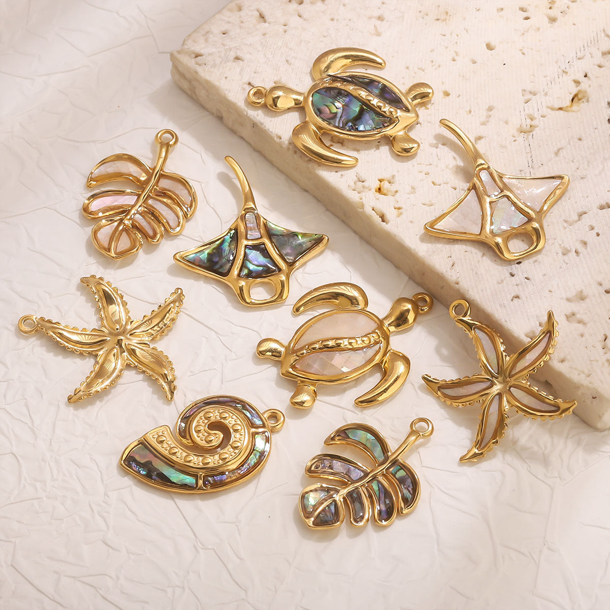 Gold and abalone shell jewelry pieces on a textured beige surface