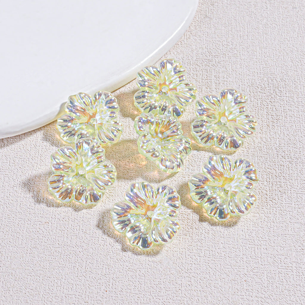 Seven iridescent resin flower beads arranged on a textured beige surface by a white plate edge